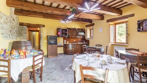 A rustic dining area with a round table set for four, wooden chairs, a kitchen area with a stove and cabinets, and a stone wall.