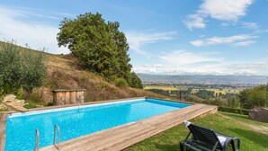 A rectangular swimming pool with a wooden deck, a bench, and a view of a distant landscape.