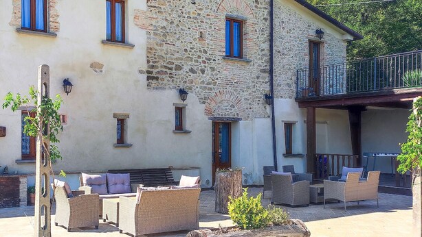 A stone building with multiple windows, outdoor seating with wicker furniture, and a log bench.