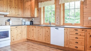 A kitchen with wooden cabinets, a dishwasher, a stove, and a window with a view of greenery. - Cozy home in Fusa with sauna (Fusa)