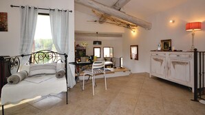 A bedroom with a bed, a window with curtains, a dining area with a table and chairs, and a white cabinet with a lamp. - 2 bedroom stunning home in Apt (Apt)