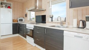 Eine moderne Küche mit Dunstabzugshaube aus Edelstahl, integriertem Backofen, Geschirrspüler und einem großen Fenster für natürliches Licht.