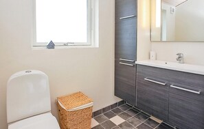 Une salle de bain avec des toilettes, un panier en osier, une fenêtre et des meubles en bois foncé.