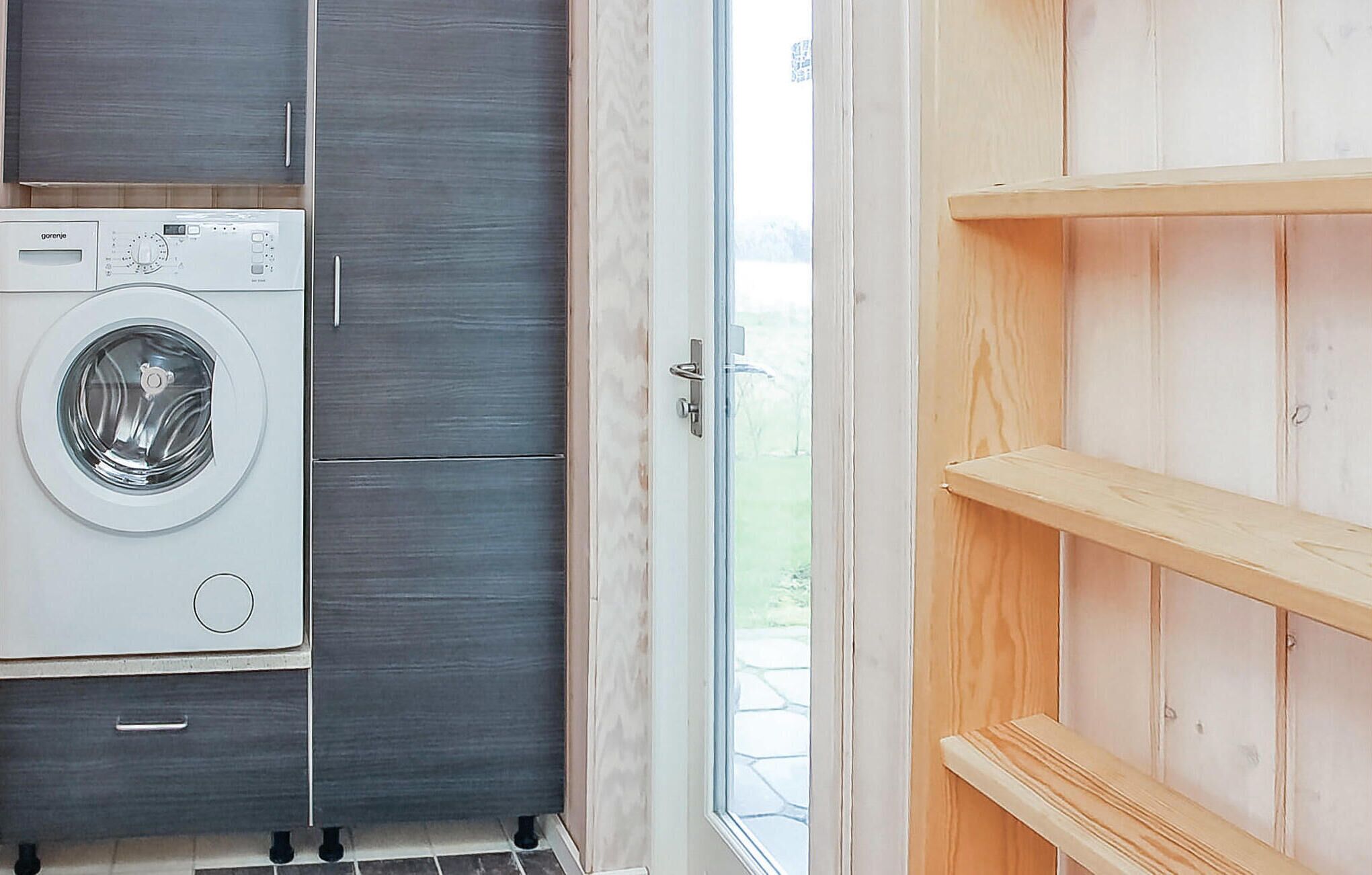 Ein Waschraum mit einer Waschmaschine mit Frontlader, einem dunklen Holzschrank und einer Holzregaleinrichtung.