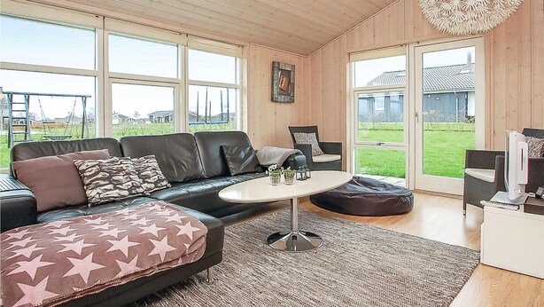 Ein modernes Wohnzimmer mit einer schwarzen Ledersofa, einem runden Couchtisch und einem großen Fenster mit Blick auf einen Garten und Häuser.
