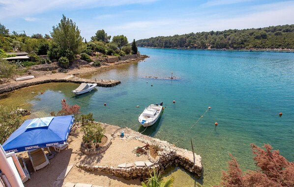 Una zona costiera con barche ormeggiate, acqua cristallina e una struttura in pietra con un ombrellone blu.