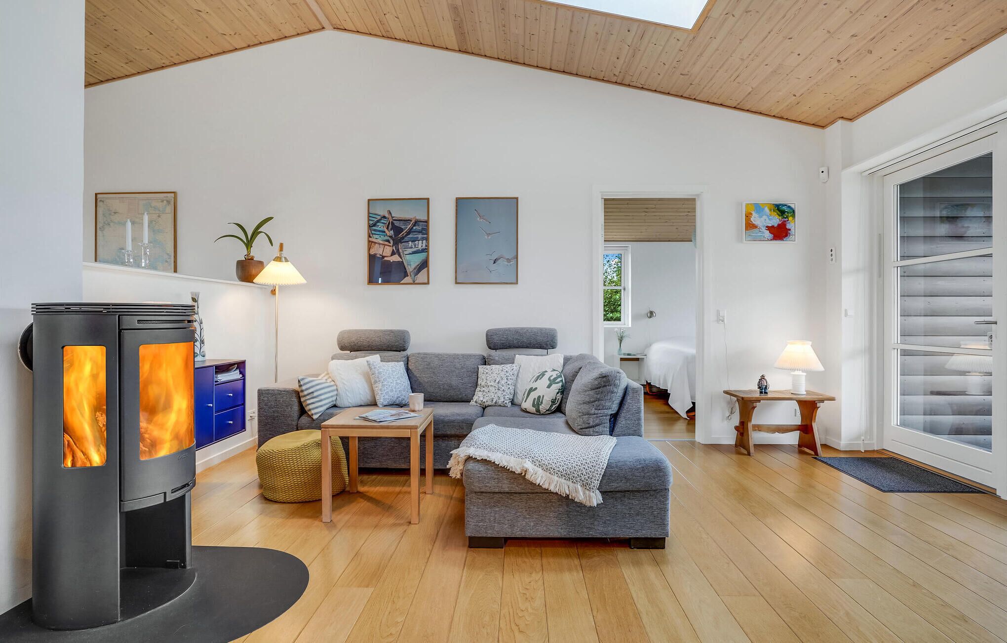 A cozy living room with a wood-burning stove, grey sofas, a coffee table, and a large window.