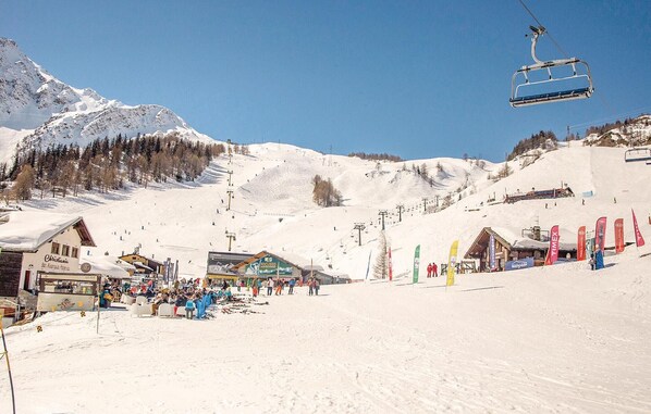 Ein Skigebiet mit Sessellift, Gebäuden und einem verschneiten Berg im Hintergrund.