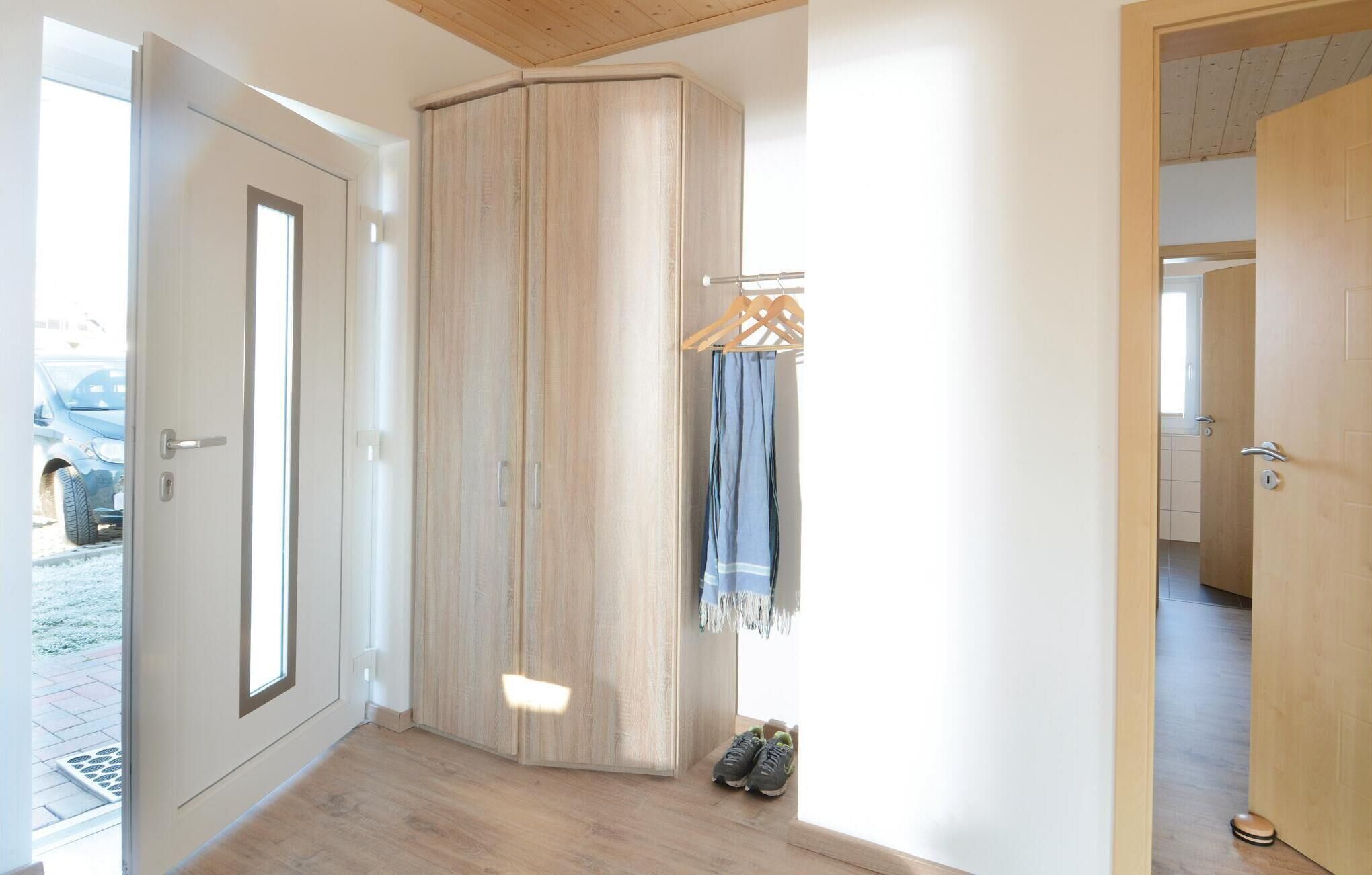 A hallway with a wooden wardrobe, a coat rack with a blue garment, and a pair of shoes on the floor.