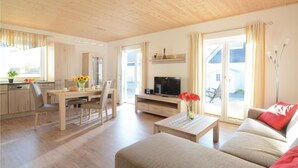 Amplia sala de estar con techo de madera, una mesa de comedor con sillas, un sofá, un televisor y una cocina con ventanal.