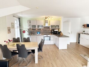 Une cuisine moderne avec des meubles blancs, un plan de travail en bois et un coin repas comprenant une table et des chaises.