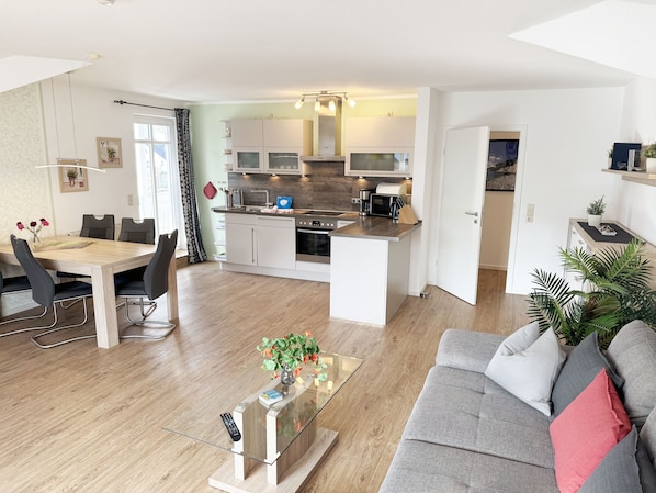 Une cuisine moderne avec des meubles blancs, un îlot central et un coin repas comprenant une table et des chaises en bois.