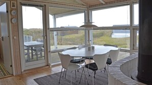 Ein moderner Essbereich mit einem runden Tisch und Stühlen, großen Fenstern mit Blick auf die umliegende Landschaft und einer Holzbalkendecke.