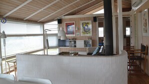 Ein Zimmer mit hoher Decke, Holzbalken, einer weißen Backsteinwand, einem schwarzen Heizkörper, einem Schreibtisch mit Computer und einem Fenster mit Jalousien.