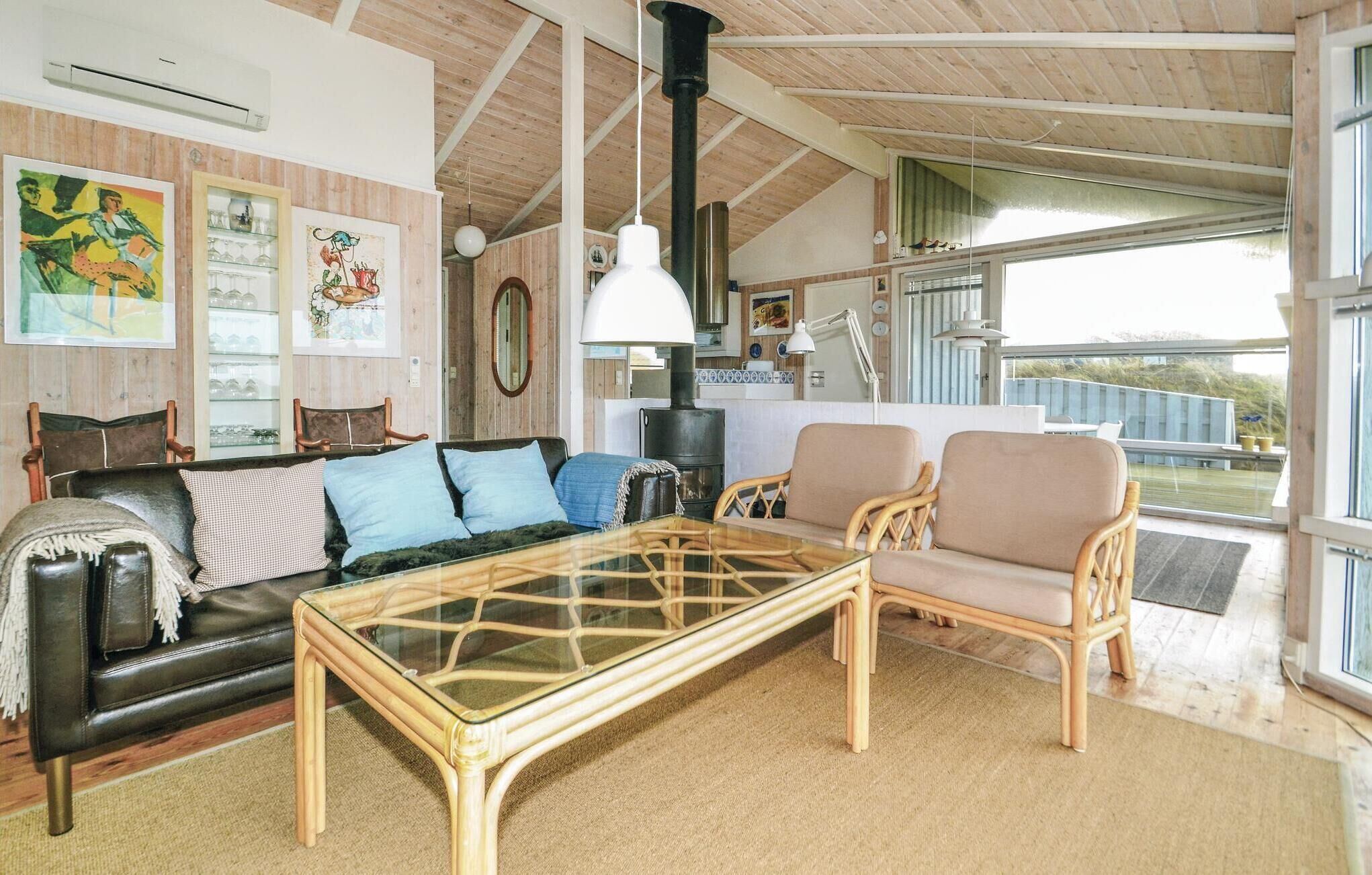 Un salon chaleureux avec une table basse en verre, un canapé en cuir et des fauteuils en osier. Une grande fenêtre offre une vue sur l’extérieur.