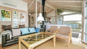 Ein gemütliches Wohnzimmer mit einem Glastisch, einer Ledersofa und Korbstühlen. Ein großes Fenster bietet einen Ausblick ins Freie.