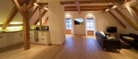 Un ampio loft con travi a vista in legno, una cucina con elettrodomestici moderni, una zona living con divano e TV, e un'ampia finestra con vista panoramica.
