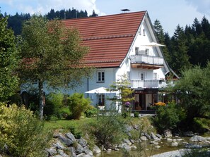 A two-story house with a red roof, white walls, and a balcony. - Apartment G1 - Apartments Garhammer, Kreuth-glassworks (Kreuth)