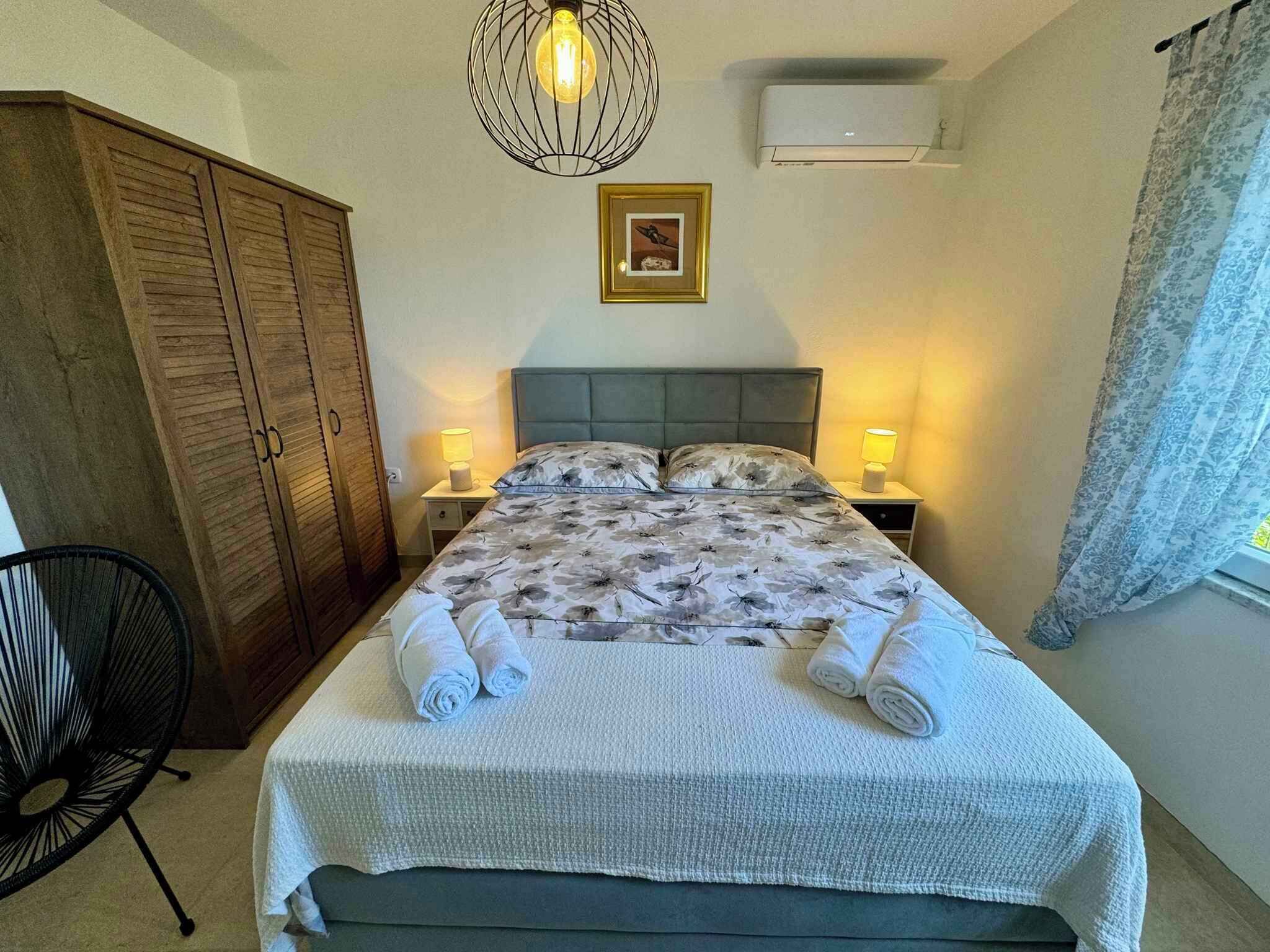 A bedroom with a bed, two bedside lamps, a wooden wardrobe, a chair, and a picture on the wall.