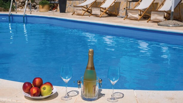 A pool area with lounge chairs, a bottle of champagne, and a plate of apples. - Awesome home in Zdrelac (Zdrelac)