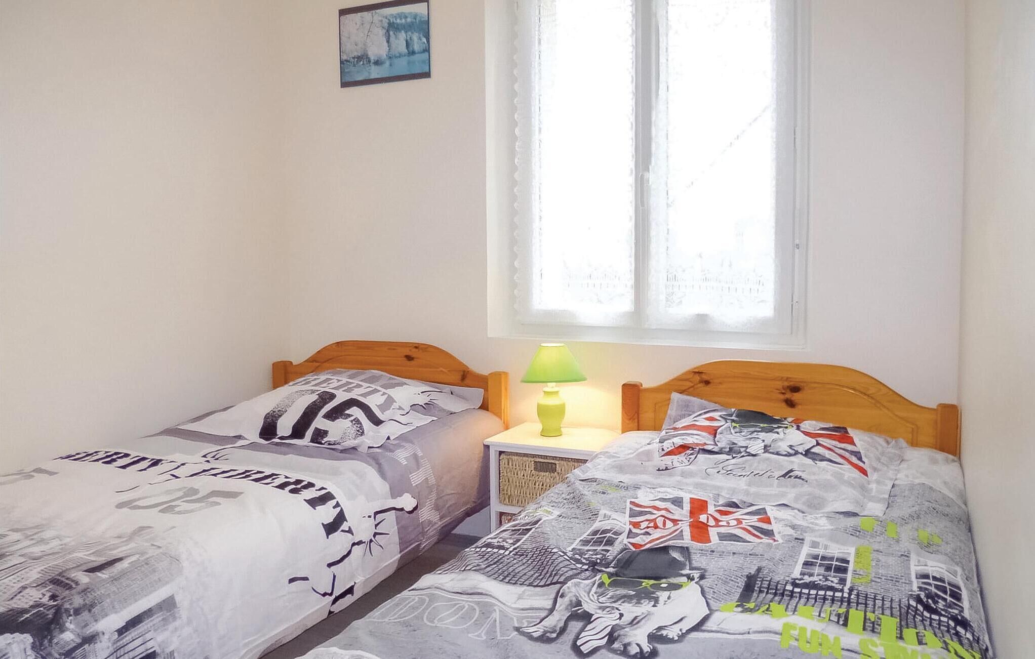 A bedroom with two single beds, a nightstand with a lamp, a window with sheer curtains, and a framed picture on the wall.