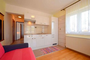 A compact kitchen with white cabinets, a stainless steel range hood, and a window with sheer curtains. - Holiday apartment mit Balkon und Meerblick (Malinska)