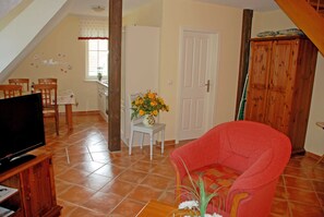 A living room with a television, a red armchair, a small table with a vase of flowers, and a dining area with chairs and a table.