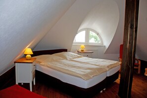 A bedroom with a single bed, a nightstand with a lamp, a window, and a radiator.
