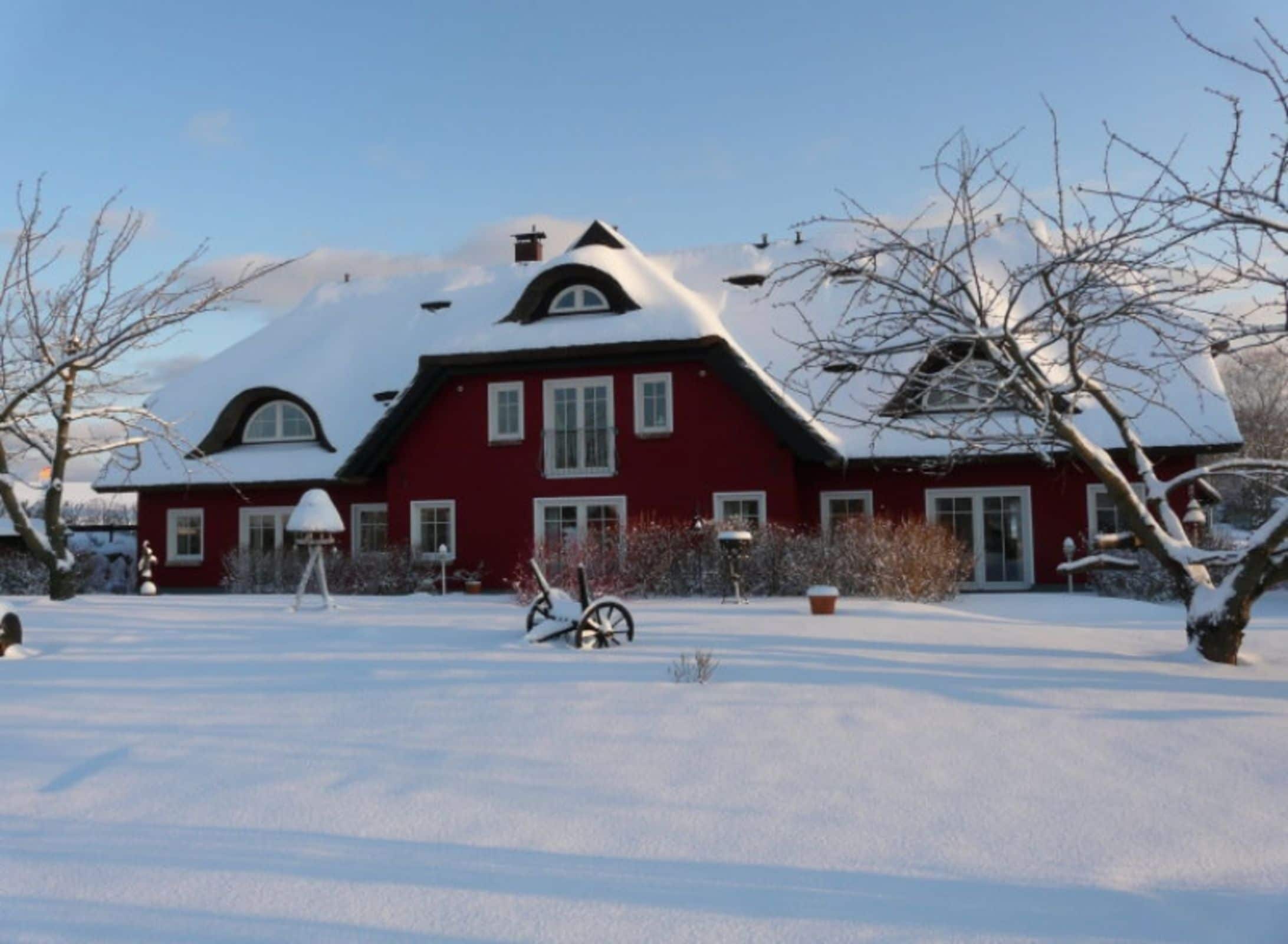 Une maison rouge, avec un toit et une cour couverts de neige.
