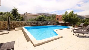 A rectangular swimming pool with a stone wall and tiled deck, surrounded by lounge chairs and a stone wall. - Holiday apartment mit Pool (Baška)