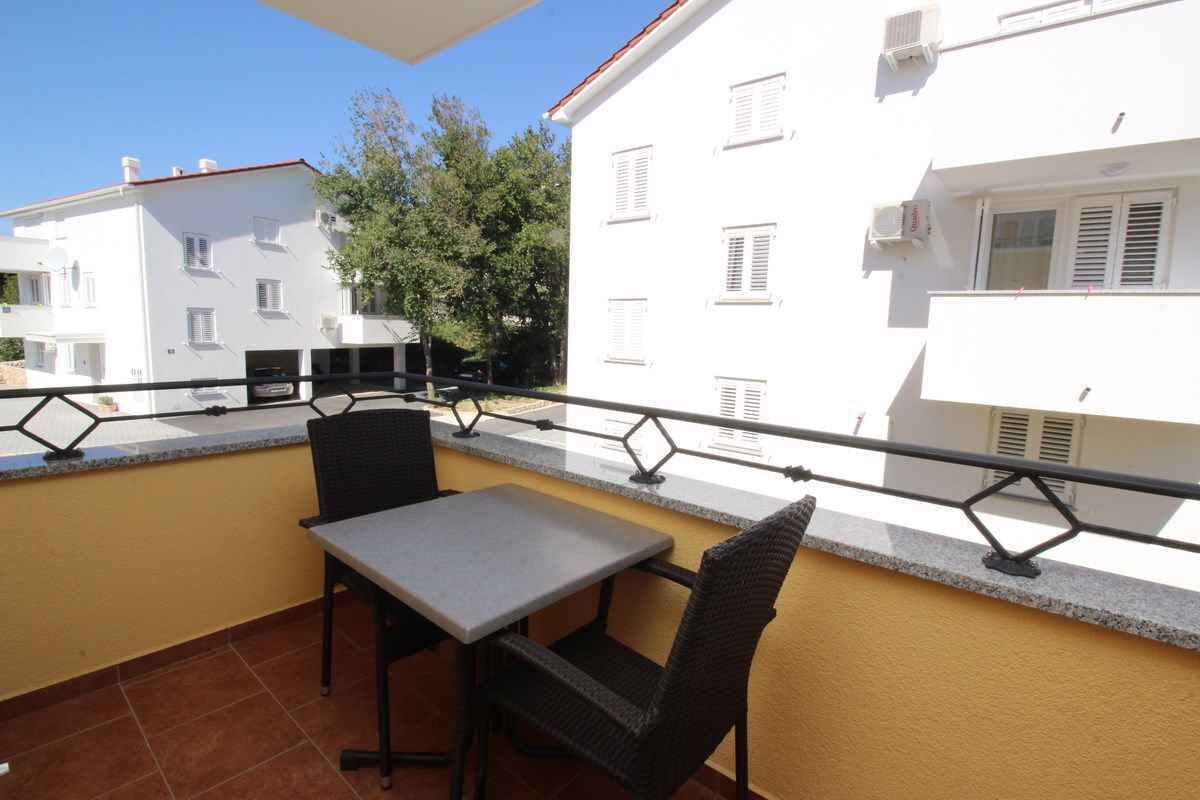 En balkon med et bord, stole, gelænder og udsigt til omkringliggende bygninger.