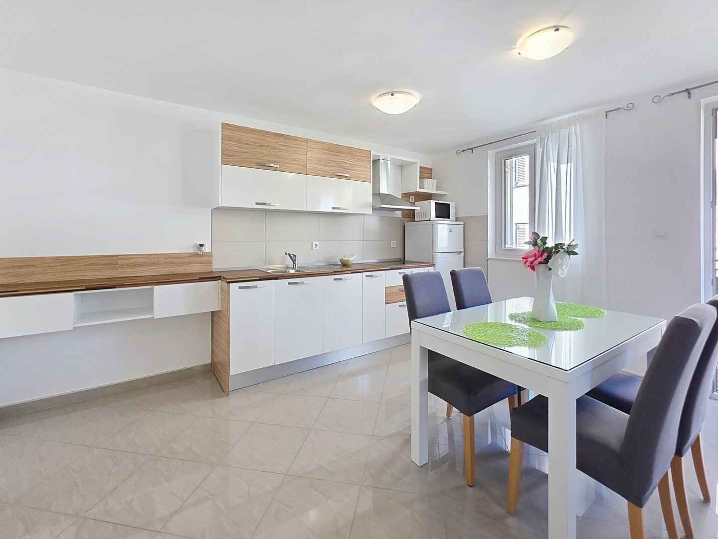 Une cuisine moderne avec des meubles blancs, un plan de travail en bois et un coin repas comprenant une table et des chaises en verre.