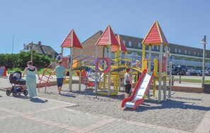 A playground with climbing structures and slides, surrounded by a paved area and buildings in the background. - 1 bedroom nice home in Ringkøbing (Ringkøbing)