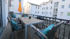 A balcony with a table and chairs, a hanging orange umbrella, and a view of adjacent buildings. - CSP: Villa Anni Whg. 06 with balcony - Villa Anni Whg. 06 with balcony (Göhren)
