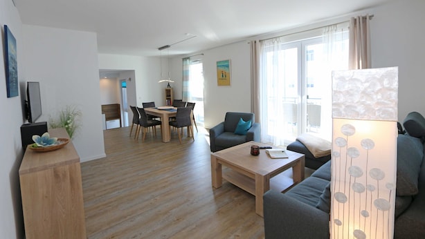 A modern living room with a wooden floor, a sofa, a coffee table, and a dining area with chairs and a table. - CSP: Villa Anni Whg. 06 with balcony - Villa Anni Whg. 06 with balcony (Göhren)