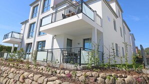 A modern two-story building with balconies, a stone retaining wall, and a clear blue sky. - CSP: Villa Anni Whg. 06 with balcony - Villa Anni Whg. 06 with balcony (Göhren)