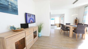 A modern kitchen with wooden cabinets, a dining area with a table and chairs, and a TV mounted on the wall. - CSP: Villa Anni Whg. 06 with balcony - Villa Anni Whg. 06 with balcony (Göhren)
