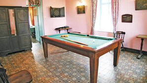 A room with a pool table, a dartboard, and a billiards cue rack.