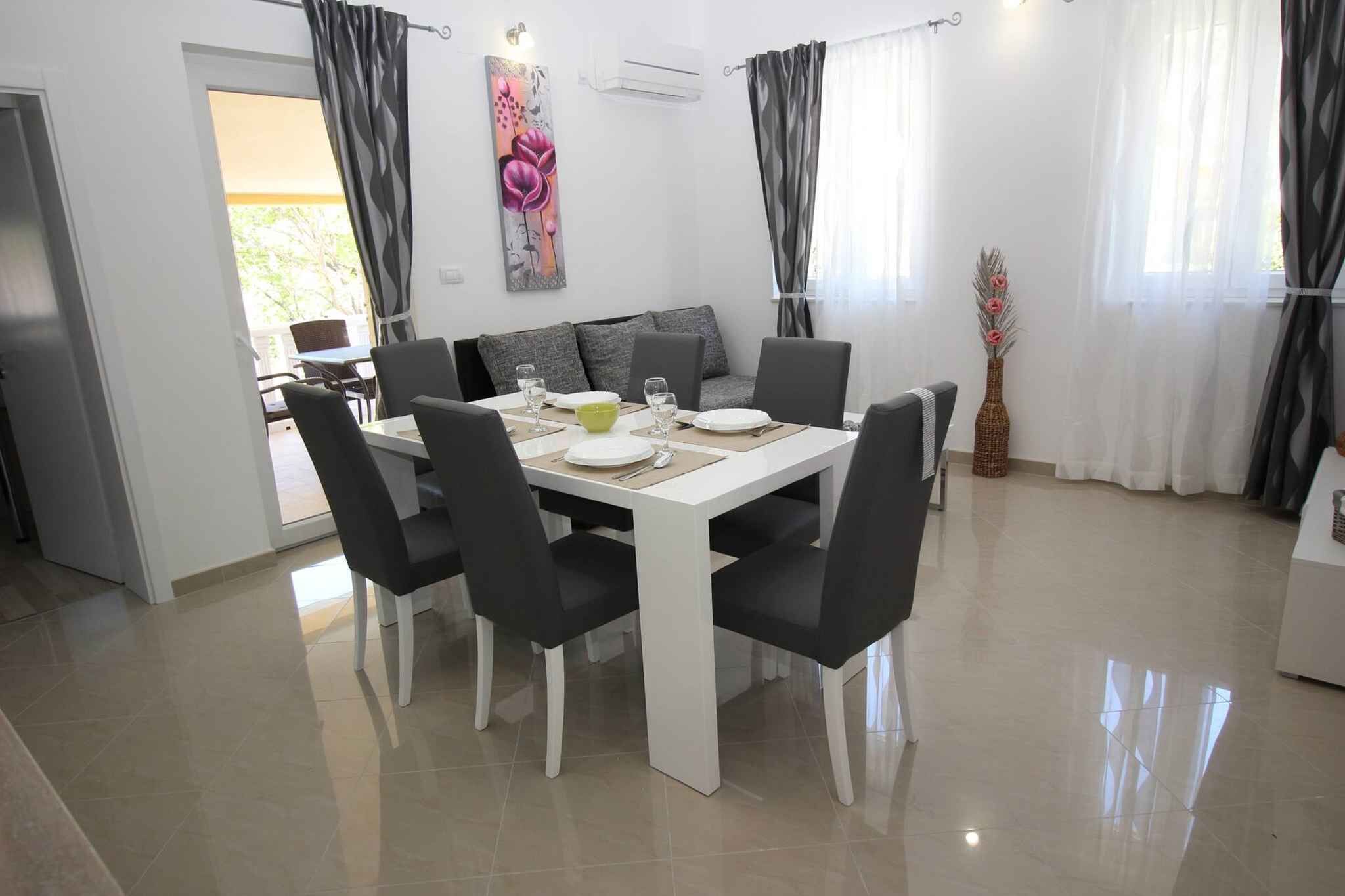 Un coin repas avec une table blanche et des chaises noires, un canapé avec des coussins et un vase rempli de fleurs.
