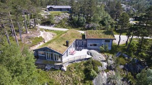 A modern house with a grass roof, situated in a mountainous area with rocky terrain and dense forest.