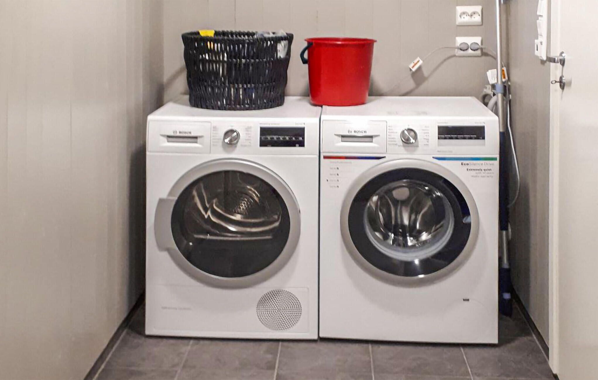 A laundry area with two front-loading washing machines and a red bucket on top.