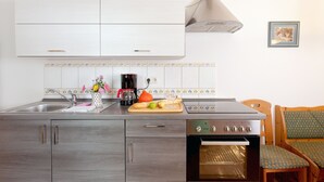 A compact kitchen with a built-in oven, a coffee maker, and a cutting board with fruits.