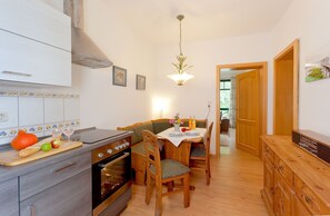 Een keuken met houten kasten, een inbouwoven, een eettafel met stoelen en een hangende lamp.
