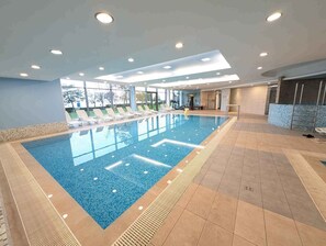Une grande piscine intérieure, dotée de nombreux transats et d’appareils de musculation en arrière-plan.