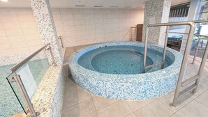 Une piscine intérieure avec un bord carrelé, une échelle en métal et un sol carrelé.