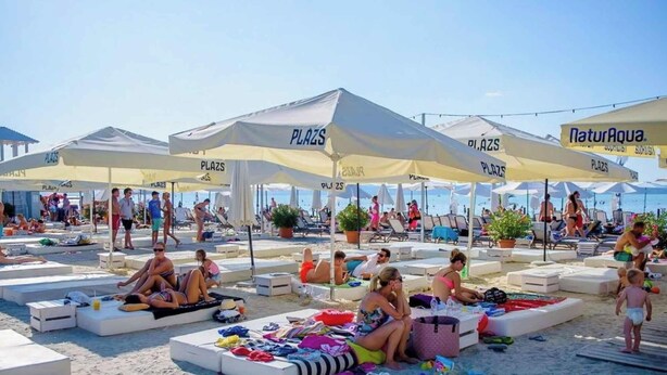 Une plage avec de nombreuses chaises longues et des parasols portant l’inscription  « PLAZS ».
