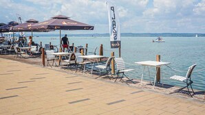 Un café situé au bord de l’eau, avec une terrasse, des tables et des parasols.