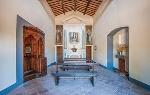 Altar area with benches and a floral arrangement, surrounded by religious paintings and a wooden cabinet.