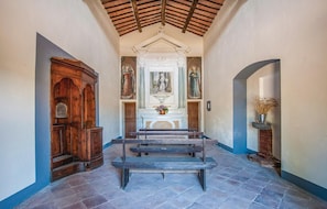 Altar area with benches and a floral arrangement, surrounded by religious paintings and a wooden cabinet.