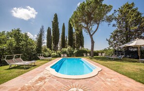 Relax by the serene pool surrounded by lush greenery and tall trees, with comfortable lounge chairs on the paved patio.